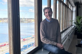 Linus sitter i fönstret på nya kontoret med Stockholms inlopp i bakgrunden