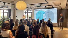 Publiken tittar på en affärspresentation om AI-sökning och SEO i ett modernt konferensrum med en stor projicerad bild och högtalare.