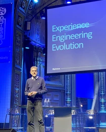 Speaker on stage beside presentation screen reading “Experience Engineering Evolution” at a conference event