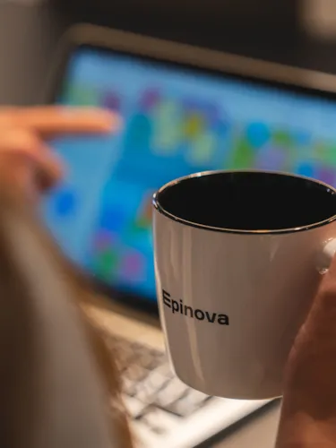 En hand som håller i en kaffekopp framför en laptopskärm
