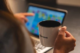 Person med kaffekopp i handen framför en datorskärm