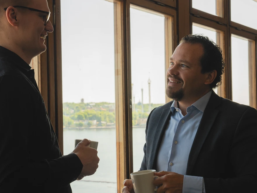 Two men talking next to a window