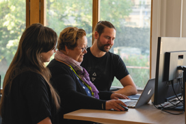 Three persons standing in front of a laptop