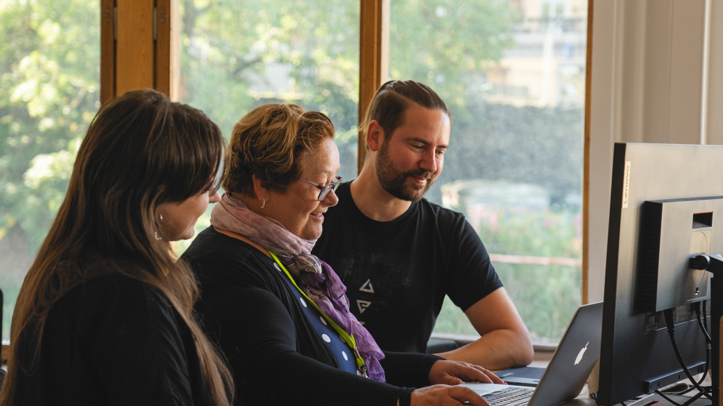 Three persons standing in front of a laptop