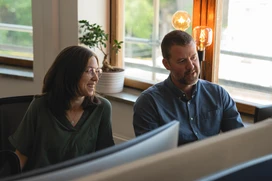 Two persons at a desk in a bright work environment discussing at a desk.