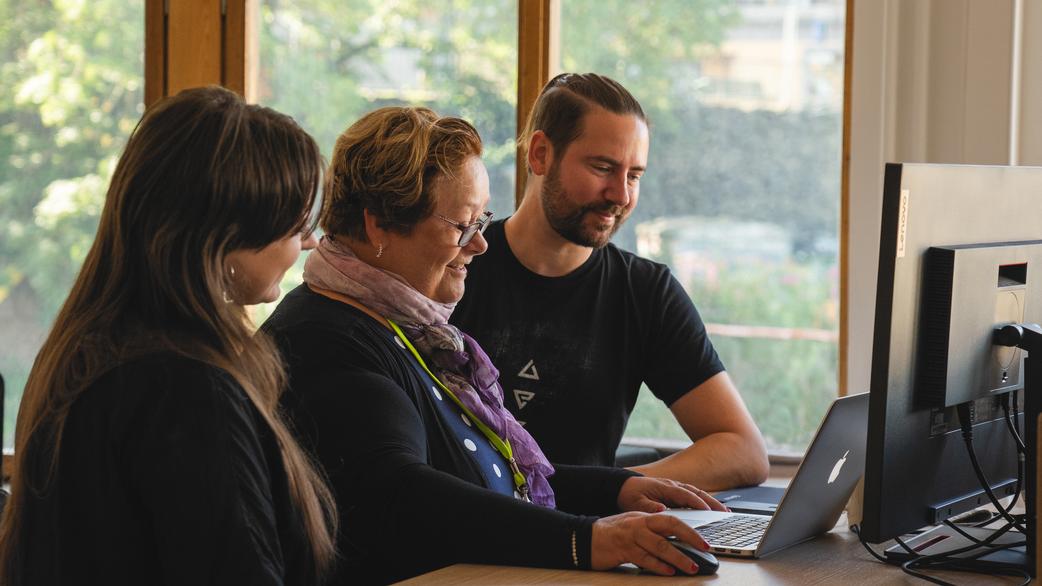 Three persons standing in front of a laptop