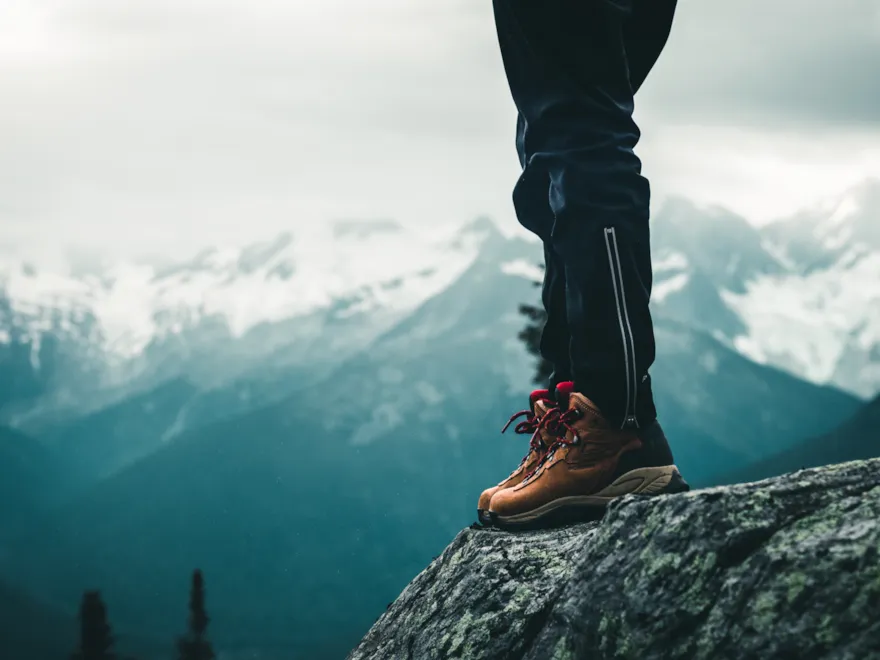 A person stands on a rock in the background high mountains