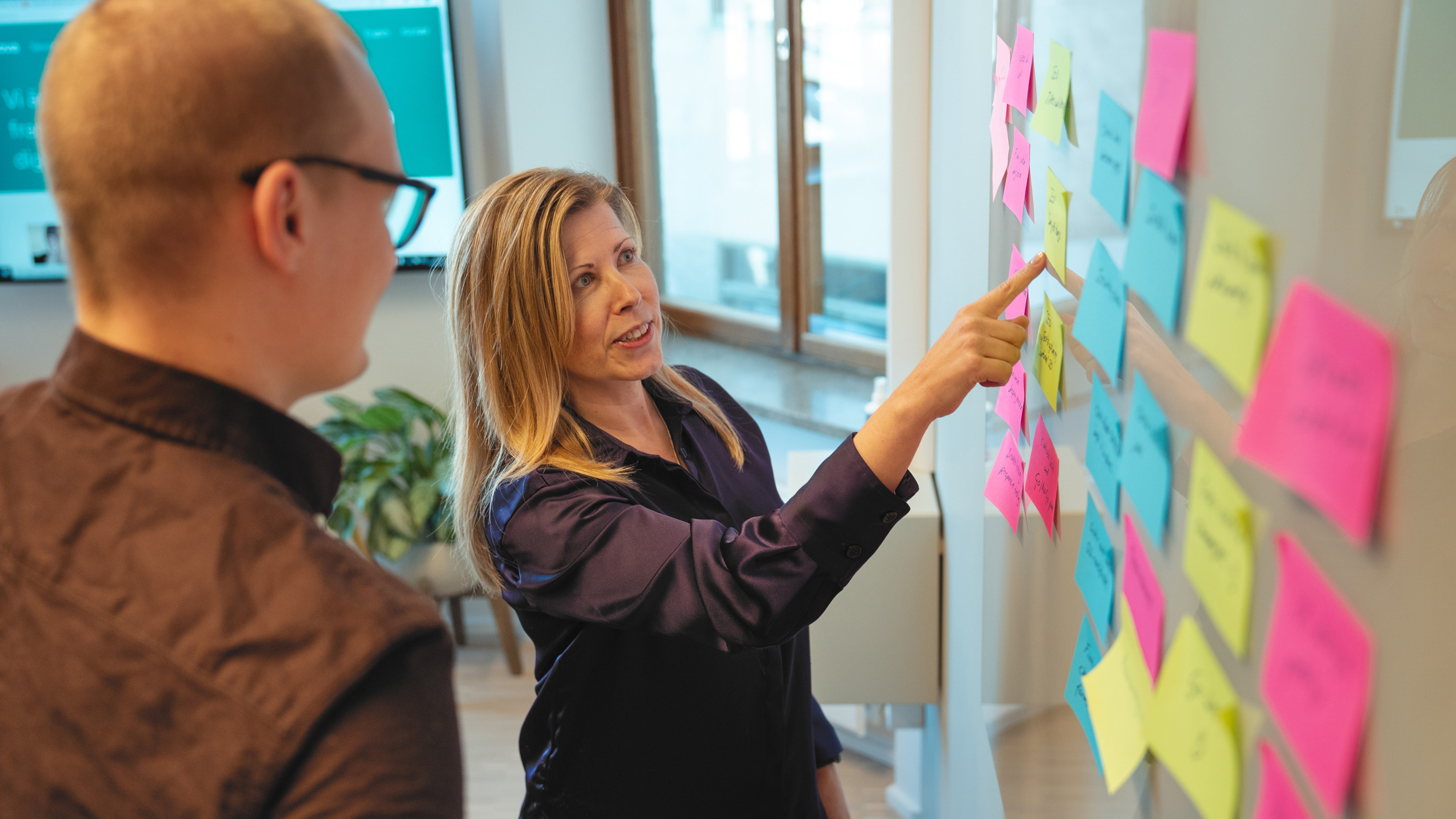 Två personer arbetar vid whiteboard-tavla med postit-lappar