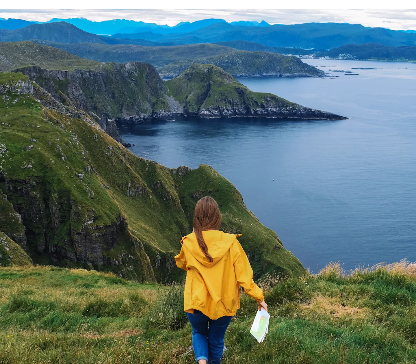 En person i gul jacka håller i en karta med utsikt över fjäll och fjord