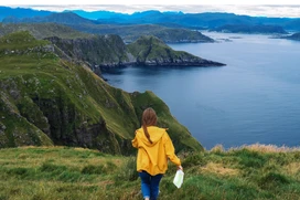 A person in a yellow jacket holds a map with a view of mountains and fjord